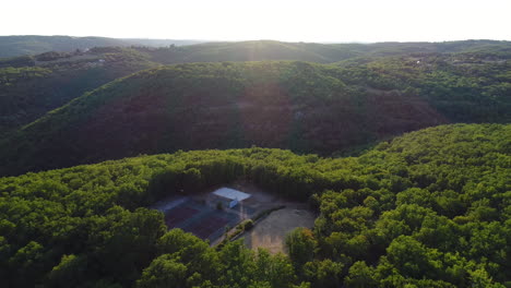 Outdoor-sports-field-in-the-middle-of-a-forest-by-aerial-drone-shot.-Sunset-time
